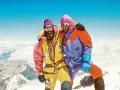 Zwei Bergsteiger auf dem Gipfel, die sich umarmen. Sie tragen bunte Daunenanzüge und Mützen. Die Frage "wie hoch ist der Mount Everest" wird hier beantwortet: 8848 Meter.