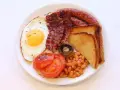 Un piatto tipico inglese con uovo fritto, bacon croccante, salsiccia, fagioli stufati, pomodori grigliati, fungo e toast.