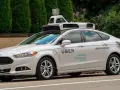 Ein weißes Uber auto mit Sensoren auf dem Dach fährt auf einer Straße.