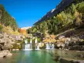Cascada en una zona de senderismo, con aguas cristalinas y árboles de otoño en las laderas rocosas.