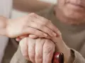 Dłoń opiekunki na dłoni starszego mężczyzny, który trzyma laskę. Wsparcie i troska, jak przy leczeniu np. chorobą Parkinsona, gdzie **Madopar** może pomóc.