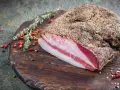 Guanciale co to? Włoski, peklowany policzek wieprzowy, pokryty pieprzem, leży na drewnianej desce z ziołami i pieprzem.