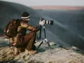 Man med ryggsäck och kamera på stativ, redo att omskola sig till naturfotograf i gryningen.