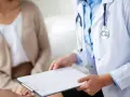 Lekarz w białym kitlu z niebieską koszulą i stetoskopem trzyma kartę pacjenta. Rozmowa o leczeniu, być może z wykorzystaniem nootropil.