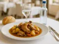 Conejo guisado con patatas y zanahorias en un plato blanco, acompañado de pan y agua.