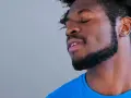 Hombre con barba cortina y cabello afro, ojos cerrados, con expresión de paz.