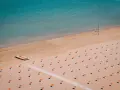 Pusta plaża w Rimini z rzędami pomarańczowych parasoli i łodzią ratowniczą.