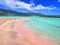 Różowy piasek plaży Elafonisi w Grecji, turkusowa woda i góry w tle.