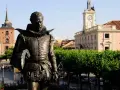 Pomnik Cervantesa w Alcalá de Henares, z ratuszem i wieżą zegarową w tle.