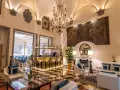 Elegant hotel lounge with a bar, fireplace, ornate chandelier, and artwork.