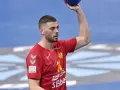 Branko Vujović, zawodnik piłki ręcznej, w czerwonej koszulce z numerem 11, trzyma piłkę nad głową.