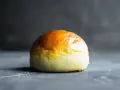 Ein goldbraunes Brioche-Brötchen liegt auf einer dunklen Oberfläche.