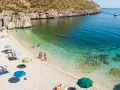 Sycylia w październiku: kamienista plaża, turkusowa woda, ludzie odpoczywają pod parasolami.