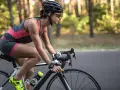 Kobieta w kasku i okularach jedzie na rowerze szosowym przez las. Widać jej nogi w sportowym stroju i zegarek na ręce. Jazda na rowerze - efekty po miesiącu są widoczne w jej sylwetce.