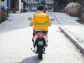 Kurier na skuterze z żółtym plecakiem Glovo jedzie ulicą.