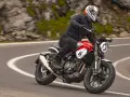 Motocyklista w kasku jedzie czerwonym motocyklem po krętej drodze. Idealny motocykl na początek przygody z jazdą.