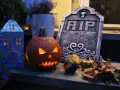 En läskig pumpa lyser upp med sitt ansikte, bredvid en gravsten och höstlöven. Perfekt för en kuslig bål halloween-kväll.