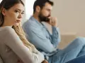 Ein Paar sitzt getrennt auf einem Sofa, die Frau wirkt nachdenklich und traurig. Ein schlechtes Gewissen nach Trennung liegt in der Luft.