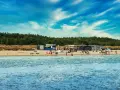 Słoneczny dzień na plaży, ludzie odpoczywają, a w tle widać budynki i las. Idealne miejsce na kemping na Helu.