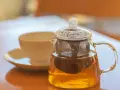 Théière en verre remplie de tisane dorée, avec une tasse en arrière-plan. La question est : combien de temps peut on garder une tisane infusée ?