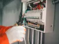 Elektryk w białych rękawicach przycina przewód do skrzynki z bezpiecznikami. Nie chce, by wybija bezpiecznik bez obciążenia.