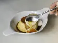 Una cuchara saca un trozo cremoso de flan de cuajada, bañado en caramelo líquido.