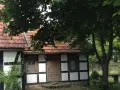 Urokliwa chata kaszubska z drewnianymi belkami i czerwoną dachówką, otoczona zielenią.