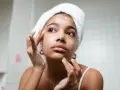 Rutina de limpieza facial: mujer con toalla en la cabeza aplica espuma en su rostro, un paso esencial para como cuidar mi piel.
