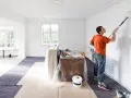 Man målar väggar, har tagit bort eluttag vid målning. Skyddsplast och färgburk syns.
