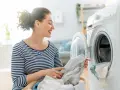 Donna sorridente carica la lavatrice, mostrando il funzionamento di un elettrodomestico moderno per il bucato.