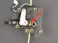 Mechanizm ekstrudera drukarki 3D, gdzie żółty filament wchodzi do mechanizmu. Strzałka wskazuje miejsce, które może wymagać czyszczenia, aby dowiedzieć się, jak wyczyścić dysze drukarki.