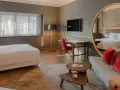 Modern hotel room with a bed, sofa, desk, and large round mirror reflecting the room.