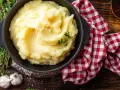 Una ciotola di cremoso purè di patate, guarnito con timo fresco, accanto ad aglio e un tovagliolo a quadri rossi.