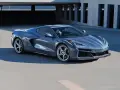 Szary Chevrolet Corvette Stingray z nowoczesnym designem, zaparkowany na tle betonowej architektury.