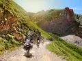Un gruppo di motociclisti affronta un emozionante giro in moto in Liguria, su una strada sterrata tra montagne verdi e rocce imponenti.