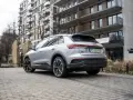 Srebrny Audi Q4 e-tron zaparkowany przed nowoczesnym budynkiem mieszkalnym.