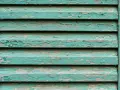 Persiane in legno fai da te con vernice verde acqua scrostata, che rivela il legno grezzo sottostante.