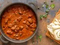Un saporito gulash di manzo in una padella, accompagnato da pane fresco e erbe aromatiche.