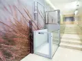 Un portal de vecinos moderno con un mural de hierbas secas y una plataforma elevadora de cristal.