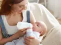 Uśmiechnięta mama karmi piersią swoje dziecko z butelki, szukając najlepszych butelek dla noworodka.