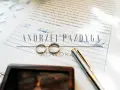 Dwa obrączki na dokumencie z podpisami i nazwiskiem "Andrzej Pazdyga", sugerujące intercyzę po ślubie. Obok pióro i drewniane pudełko.