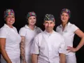 Cztery osoby w białych uniformach i kolorowych czepkach na czarnym tle.