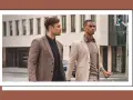 Dos hombres con trajes elegantes caminan por la calle. Uno lleva un traje beige y el otro un traje marrón.