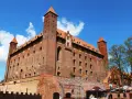 Potężny zamek w Gniewie, ceglana twierdza z wieżami i czerwonymi dachami, pod błękitnym niebem. Ciekawostki o jego historii czekają na odkrycie.