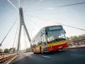 Żółto-czerwony autobus elektryczny Yutong U12 jedzie po moście nad rzeką.