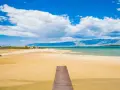 Drewniany pomost prowadzi na piaszczystą plażę Ninskiej laguny. W tle turkusowe morze i góry.