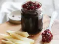 Un vasetto di marmellata di cipolle scura, con un cucchiaino che ne raccoglie una porzione, accanto a fette di formaggio stagionato.