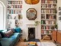 Acogedor salón estrecho y rectangular con sofá azul, chimenea y estanterías repletas de libros.