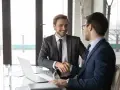 Uśmiechnięty mężczyzna w garniturze proponuje przejście na ty, ściskając dłoń partnerowi biznesowemu.