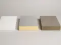 Trzy próbki materiałów budowlanych: biały styropian, płyta warstwowa z pianką i okładziną, oraz szara wełna mineralna. Wszystkie służą do izolacji cieplnej.